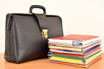 Retro black leather briefcase and stack of files on the brown wooden table. Focus on the briefcase. 