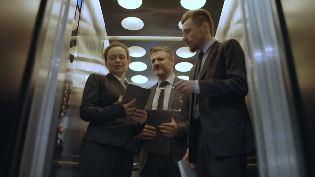 Corporate employees talking while exiting elevator, atmosphere in office building