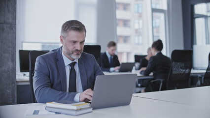 Serious concentrated man in business suit typing on laptop sitting in office