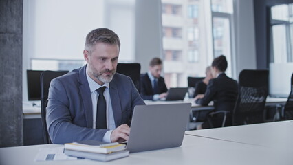 Serious concentrated man in business suit typing on laptop sitting in office - Powered by Adobe