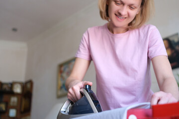 Happy woman ironing clothes with electric iron at home