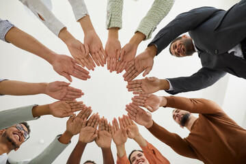 Closeup downward view of diverse international people join hands in circle motivated for shared...