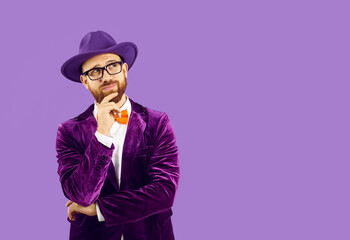 Portrait of funny curious man with ginger beard, wearing hat and eyeglasses, puts hand on chin while looking away at blank solid purple copyspace background on right side, reading text and thinking