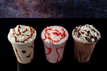 Milkshakes of different flavors in clear glass on a dark background.