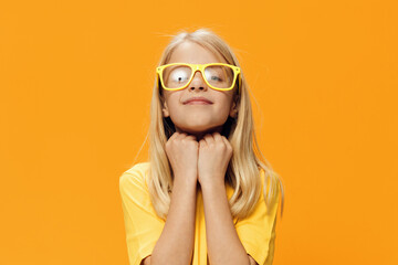a cute, funny girl, of school age, stands on a yellow background in a yellow T-shirt in yellow glasses, posing funny. Horizontal studio photography with blank space for advertising mockup