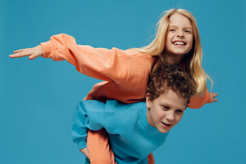 happy joyful children, brother and sister of school age play together and the boy rolls the girl on his back. Horizontal studio photography on a blue background
