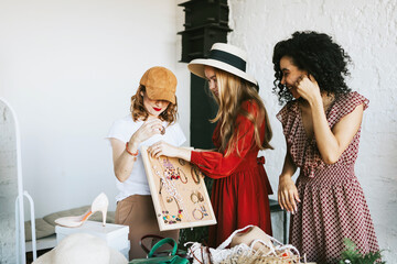 three young woman female caucasian and african students at swap party try on clothes, bags, shoes and accessories, change clothes with each other, second hand for things, zero waste life, eco-friendly