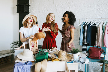 three young woman female caucasian and african students at swap party try on clothes, bags, shoes...