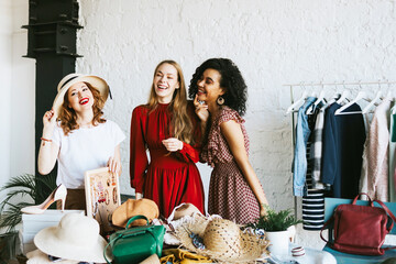 three young woman female caucasian and african students at swap party try on clothes, bags, shoes and accessories, change clothes with each other, second hand for things, zero waste life, eco-friendly