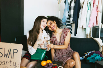 two young woman female caucasian and african students at swap party try on clothes, bags, shoes and...