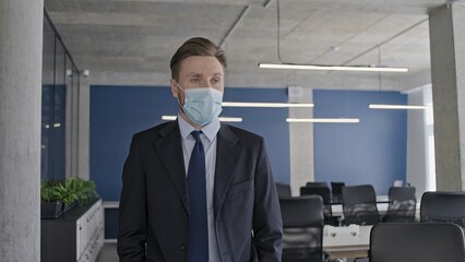 Sad businessman in face mask looking at empty office, pandemic impact on company