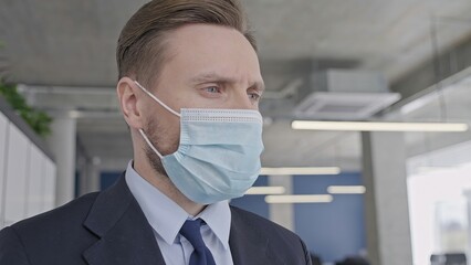 Fototapeta na wymiar Depressed businessman in protective face mask standing in empty office, covid-19 pandemic