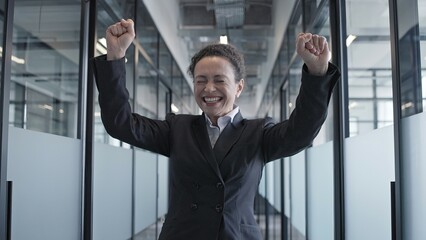 Happy woman in business suit dancing in office corridor, celebrating success