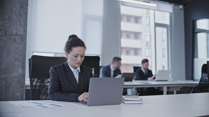 Woman office worker typing on laptop, sitting in business office, working on a project
