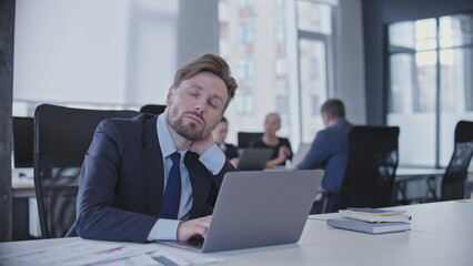 Sleepy male manager sitting at workplace in business office, tired of overworking