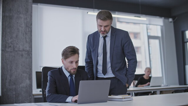 Male boss supervising work of newbie office manager, giving advice, internship