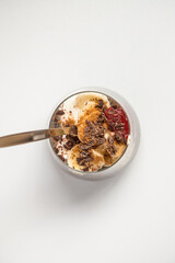 Chia seeds from the Salvia hispanica plant. Glass cup with hydrated seeds, natural yogurt, banana, strawberry jam, cinnamon powder and chocolate shavings. Image seen from above on white background.