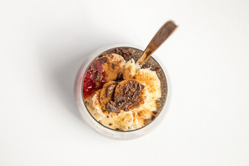 Chia seeds from the Salvia hispanica plant. Glass cup with hydrated seeds, natural yogurt, banana, strawberry jam, cinnamon powder and chocolate shavings. Image seen from above on white background.