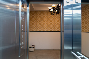 interior de elevador con puerta abierta y botonera con candil al fondo y pared con papel tapiz