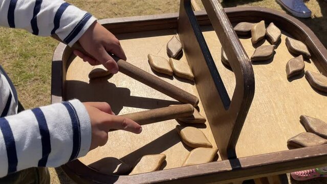 close-up of the hands of a boy playing a wooden game in which it is necessary to take wooden figurines with chopsticks