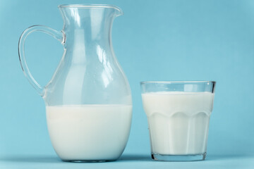 Jug and glass full of milk on blue background. Benefits of dairy products concept