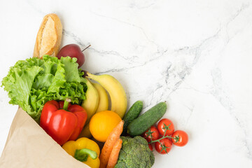 Grocery brown paper bag full of fresh fruits and vegetables on white marble background. Shopping and delivery service concept. Healthy food diet concept. Free space. Flat lay
