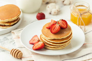 American pancakes decorated with strawberries and sprinkled with powdered sugar in a white plate. Healthy and tasty breakfast