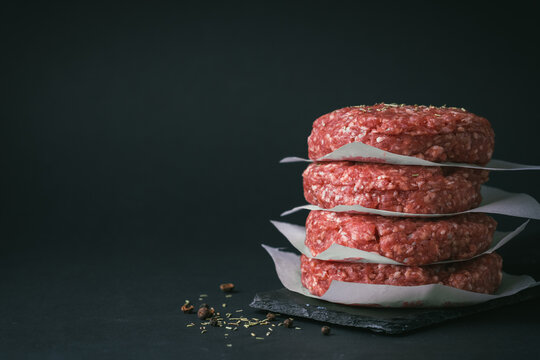 Raw ground beef burger patties separated by parchment paper on a black background