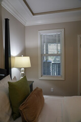 View of a bed, lamp on nightstand, window and crown molding.