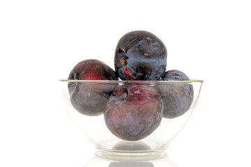 Several ripe black plums in glassware, close-up, isolated on a white background.