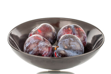 Several ripe black plums in a black ceramic plate, close-up, isolated on a white background.