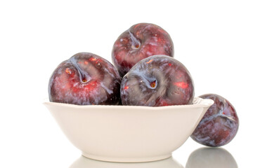 Several ripe black plums in a white ceramic plate, close-up, isolated on a white background.