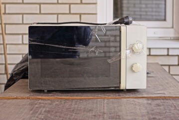 one old black white broken electric microwave stand on a brown table against a brick wall outside