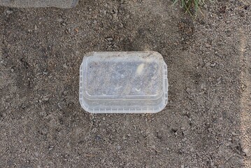 garbage from one empty plastic white box lies on gray ground in the street