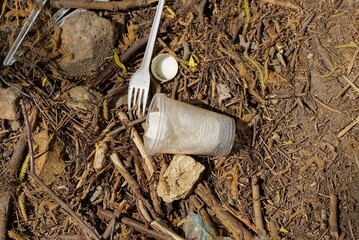 garbage from one empty white plastic cup and fork lies on the brown ground in  nature