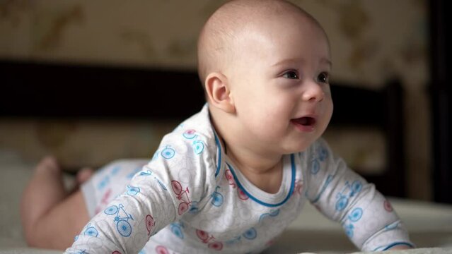 Newborn Active Baby Cute Smiling Teethless Face Portrait Early Days On Stomach Developing Neck Control. 5 Months Child On White Bed Looking on Camera. Infant, Childbirth, Parenthood, Beginning Concept