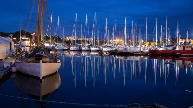 Sailboats in port on a windless night. Reflections in water.
