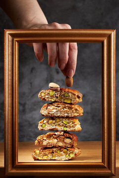 Female hand takes sweet fresh italian cookies cantuccini with pistachios and almonds from stack in a wooden frame against dark background