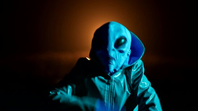Hilarious alien dancing on dark backdrop. Funny meme footage of arrived on extraterrestrial planet masquerading as human person in smooth raincoat. UFO, fantasy, futuristic, fiction concept.