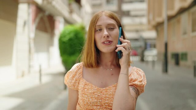 Young redhead woman smiling confident talking on the smartphone walking at street