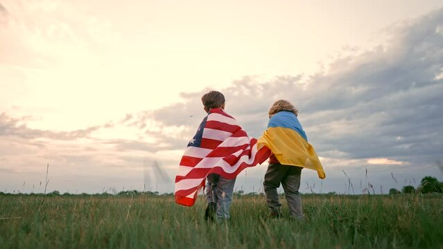 Ukrainian and american boys - patriot children running together with national flags on open area field. USA and Ukraine friendship. Country partners, support. Independence day, celebration.