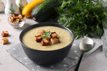 Creamy soup from chicken and zucchini served with white bread croutons in dark bowl on gray background