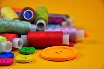 Set of buttons and Spools with multicolored threads on a yellow background. Blurring background.