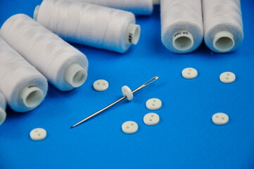 Set of White buttons and Spools threads on a blue background.