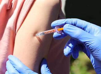 doctor with gloves while administering the vaccine on the arm of the young student during the...