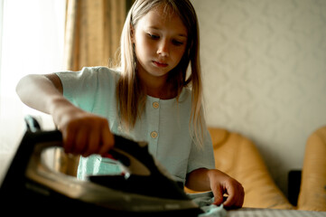 A 6-7-year-old girl helps her mother around the house, she irons clothes with an iron. The child is taught to order.