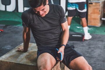 Young Latin man resting after his crossfit exercise routine. With smartphone in his hand
