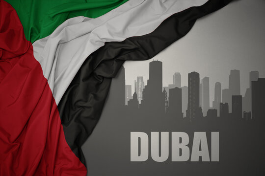 abstract silhouette of the city with text Dubai near waving national flag of united arab emirates on a gray background.