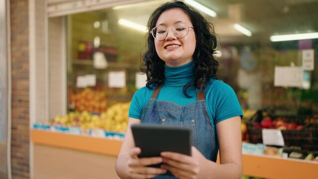 Young chinese woman employee smiling confident holding data phone at fruit store