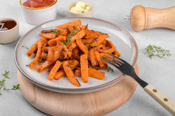 Tasty homemade roasted sweet potato with herbs, salt and pepper roasted in the pan on a ceramic plate and mayo, on a light grey table background, close up